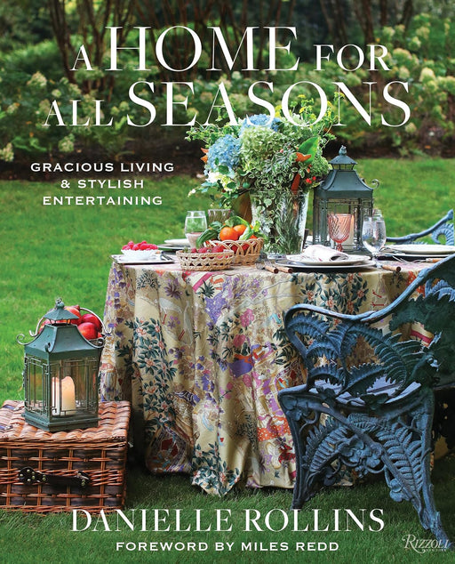 Book cover of 'A Home for All Seasons' by Danielle Rollins, featuring an outdoor setting with a table and floral arrangements.
