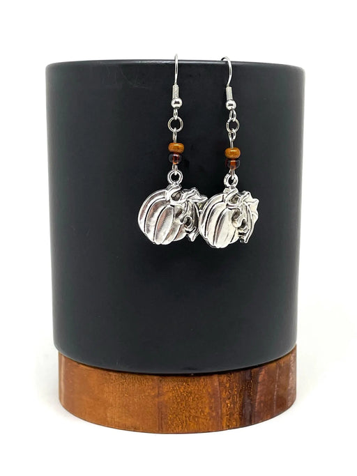 Pair of silver earrings with pumpkin charms on a black cylindrical stand with wooden base.