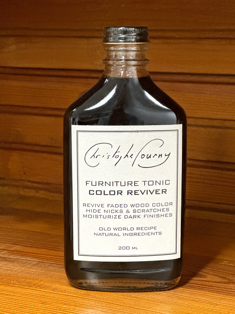 A glass bottle labeled 'Furniture Tonic Color Reviver' placed on a wooden surface.