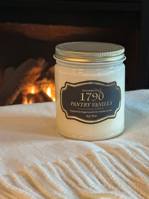 Jar of '1790 Pantry Vanilla' candle on a textured surface with a fireplace in the background
