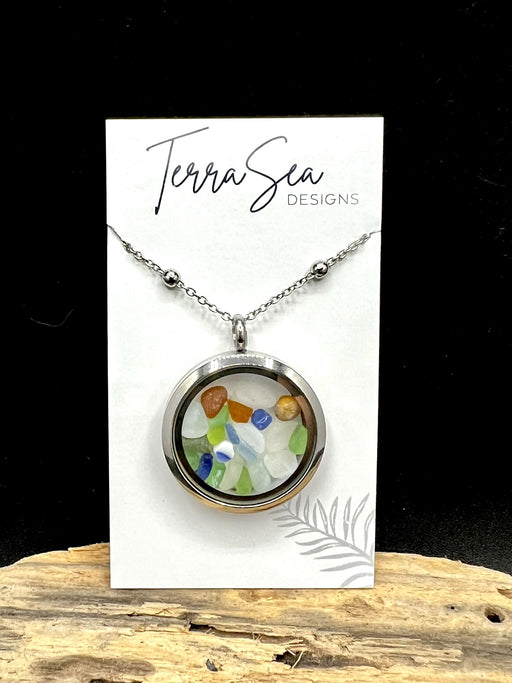 A stainless steel locket with colorful seaglass gems and shells, displayed on a card with the brand name 'Terrasea Designs'.