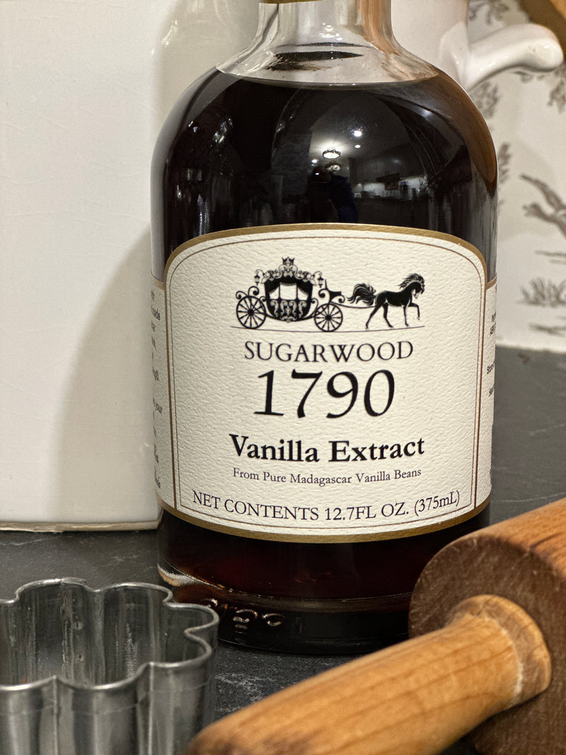 Bottle of Sugarwood 1790 Vanilla Extract on a white surface with a wooden spoon in the background.
