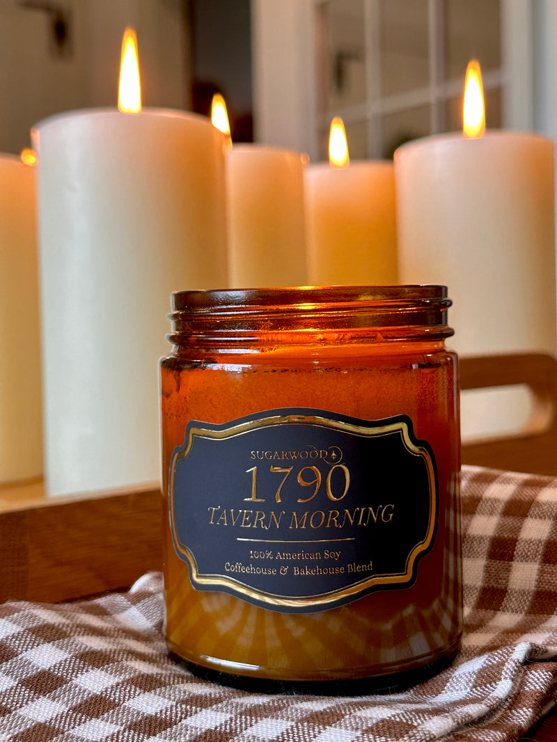Candle jar labeled '1790 Tavern Morning' with lit candles in the background