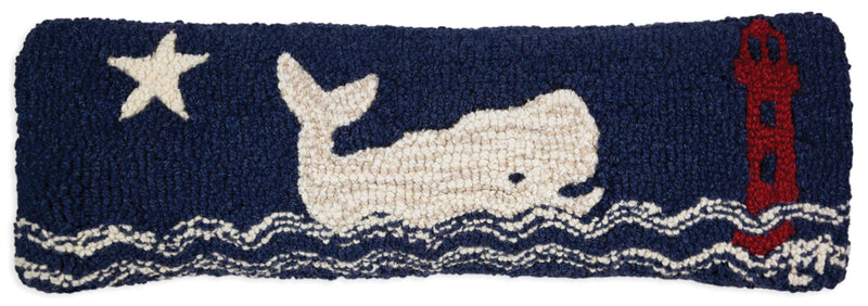 A rectangular, hand-hooked wool pillow with a dark blue background featuring a white whale, red life buoy, and white star, designed to represent a nautical theme.