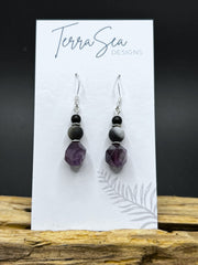 A pair of earrings featuring amethyst, amazonite, and black jasper beads, displayed on a card with 'Terra Sea Designs' printed on it.