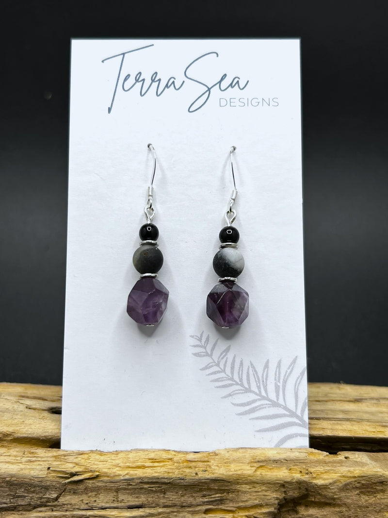 A pair of earrings featuring amethyst, amazonite, and black jasper beads, displayed on a card with 'Terra Sea Designs' printed on it.