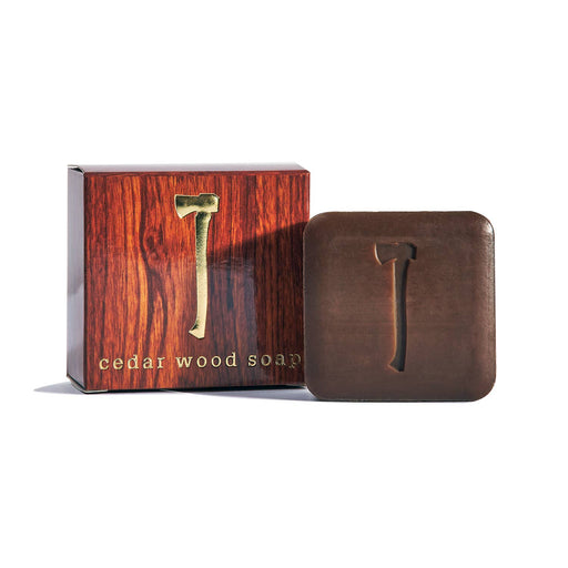 A bar of cedar wood soap placed in front of its wooden packaging box with a handle design.