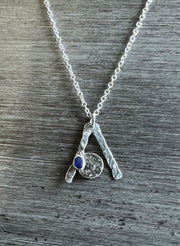 A sterling silver necklace with a cobalt blue seaglass pendant on a silver plated chain, displayed against a textured grey background.