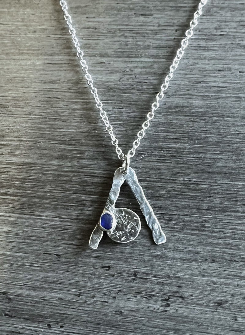 A sterling silver necklace with a cobalt blue seaglass pendant on a silver plated chain, displayed against a textured grey background.
