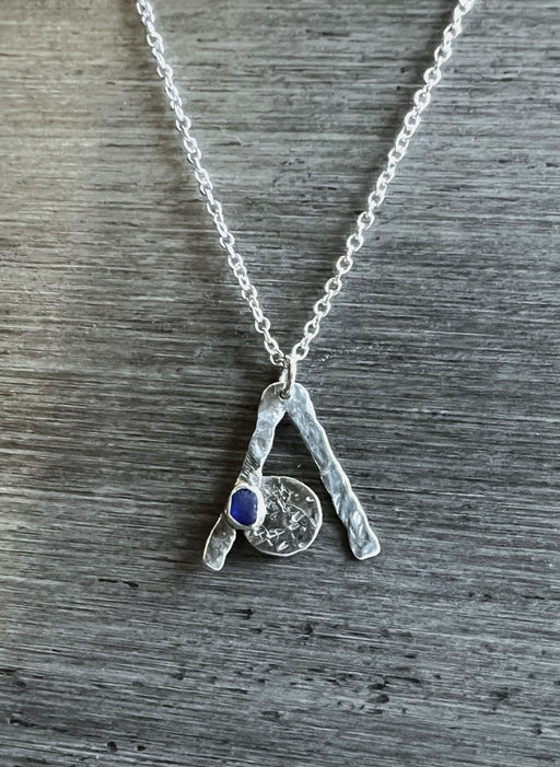 A sterling silver necklace with a cobalt blue seaglass pendant on a silver plated chain, displayed against a textured grey background.