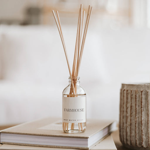 A Farmhouse reed diffuser with clear glass and wooden reeds, placed on a stack of books, filling the room with a fall fragrance.