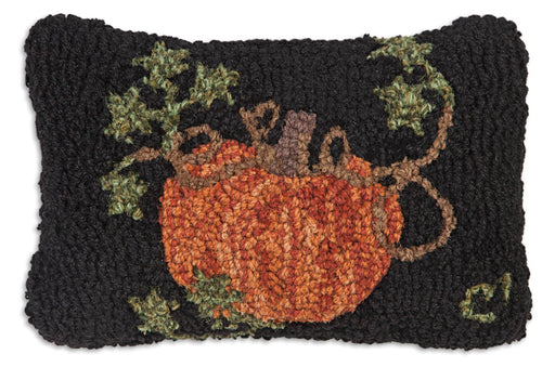 A hand hooked wool pumpkin pillow with a black background featuring a orange pumpkin and green leaves design, made with a velveteen backing and poly-fill pillow insert.