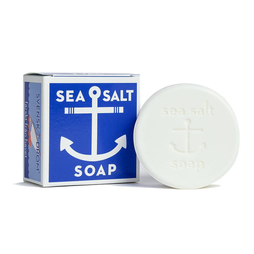 A round bar of soap with 'Sea Salt Soap' engraved on it, placed next to a rectangular blue and white box with the same text and an anchor symbol.