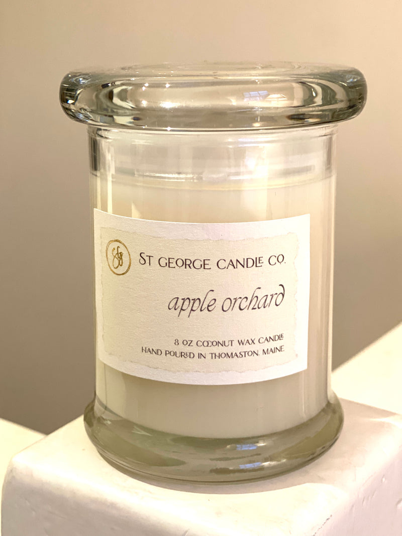 A clear glass jar candle with a label reading 'St George Candle co. apple orchard', containing a white cylindrical candle.